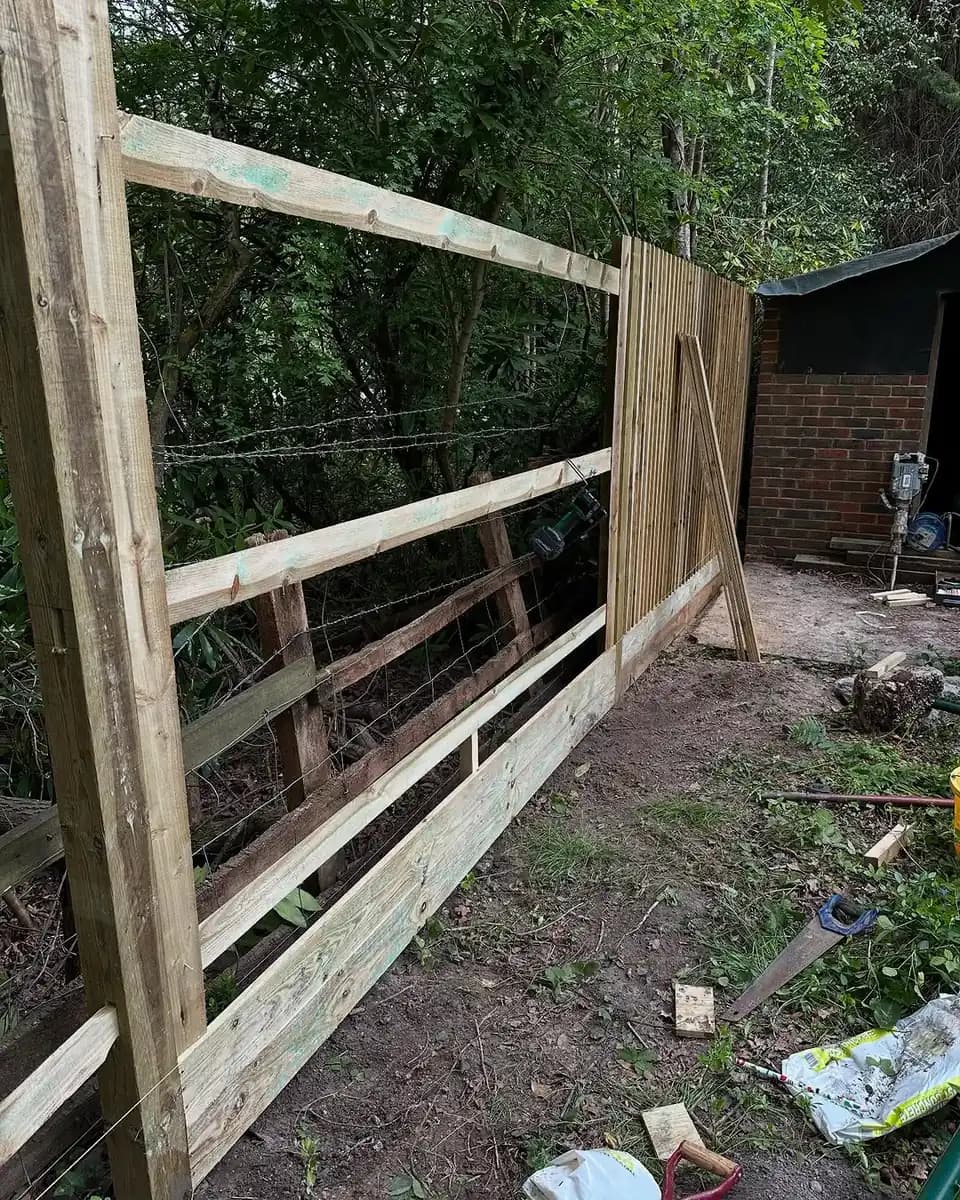 Post-and-rail fencing installation underway along a wooded boundary.